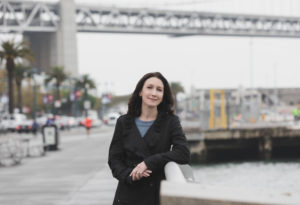 Elaine Pofeldt leaning against a rail near water with bridge in background