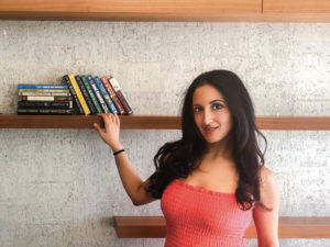 Paula in coral dress in front of bookshelf
