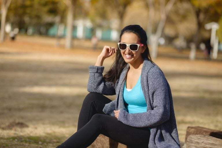 Photo of Paula Pant wearing sunglasses sitting on a piece of wood