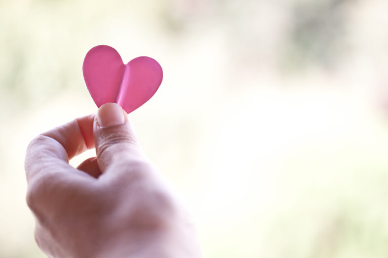 Photo of a hand holding a cut-out pink heart
