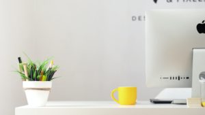 A desk with a small plant, yellow cup, and imac on it